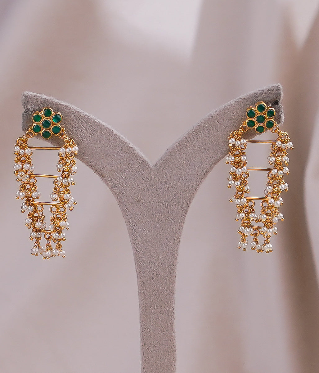 Gold earrings with green gemstones and pearl drops, displayed on a stand