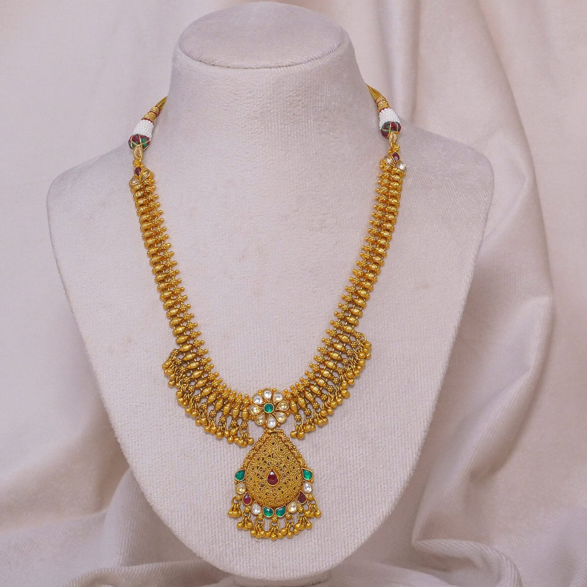 Elegant gold necklace with intricate design, red and green gemstones, displayed on mannequin