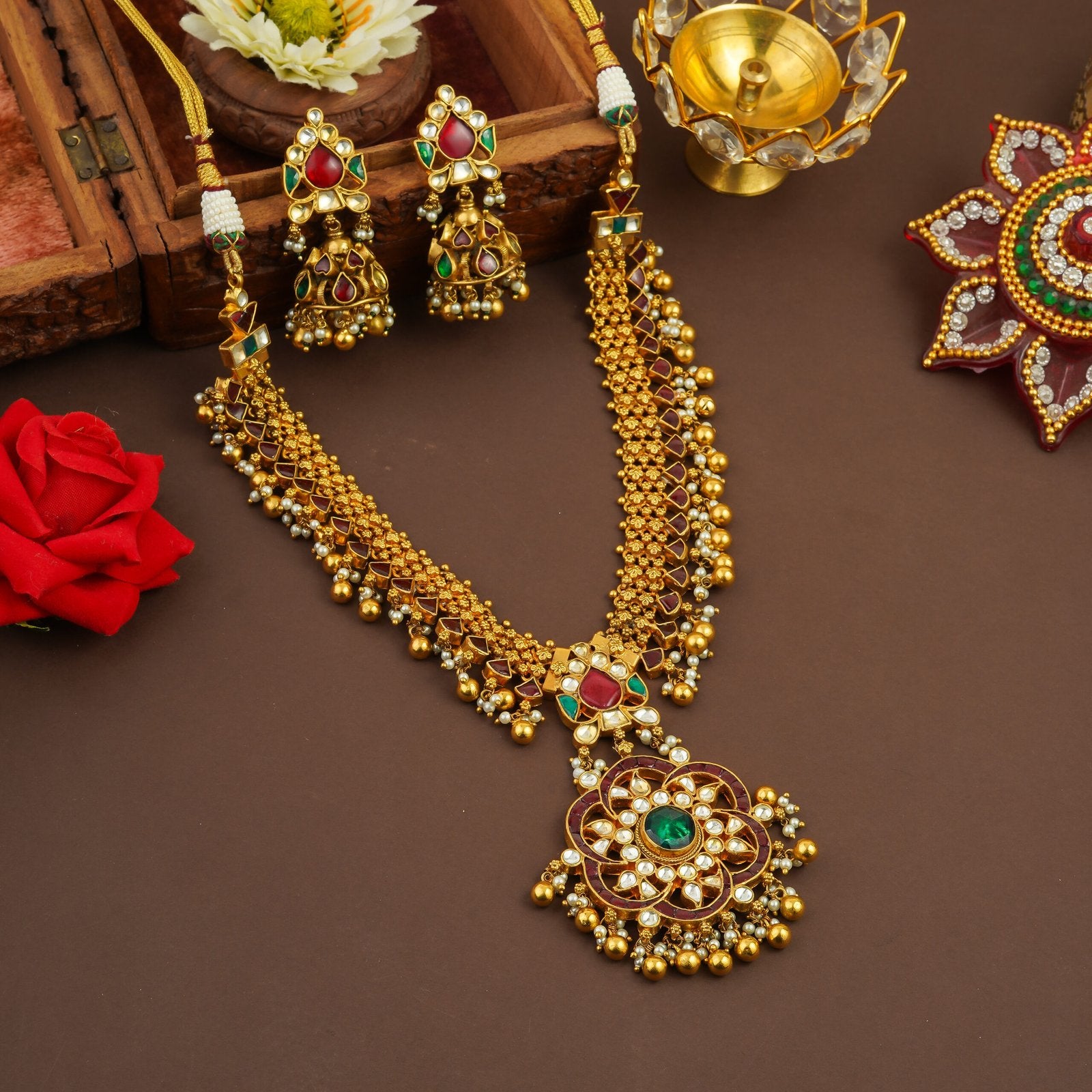 Elegant gold necklace set with red and green gemstones, paired with matching earrings and floral decor.