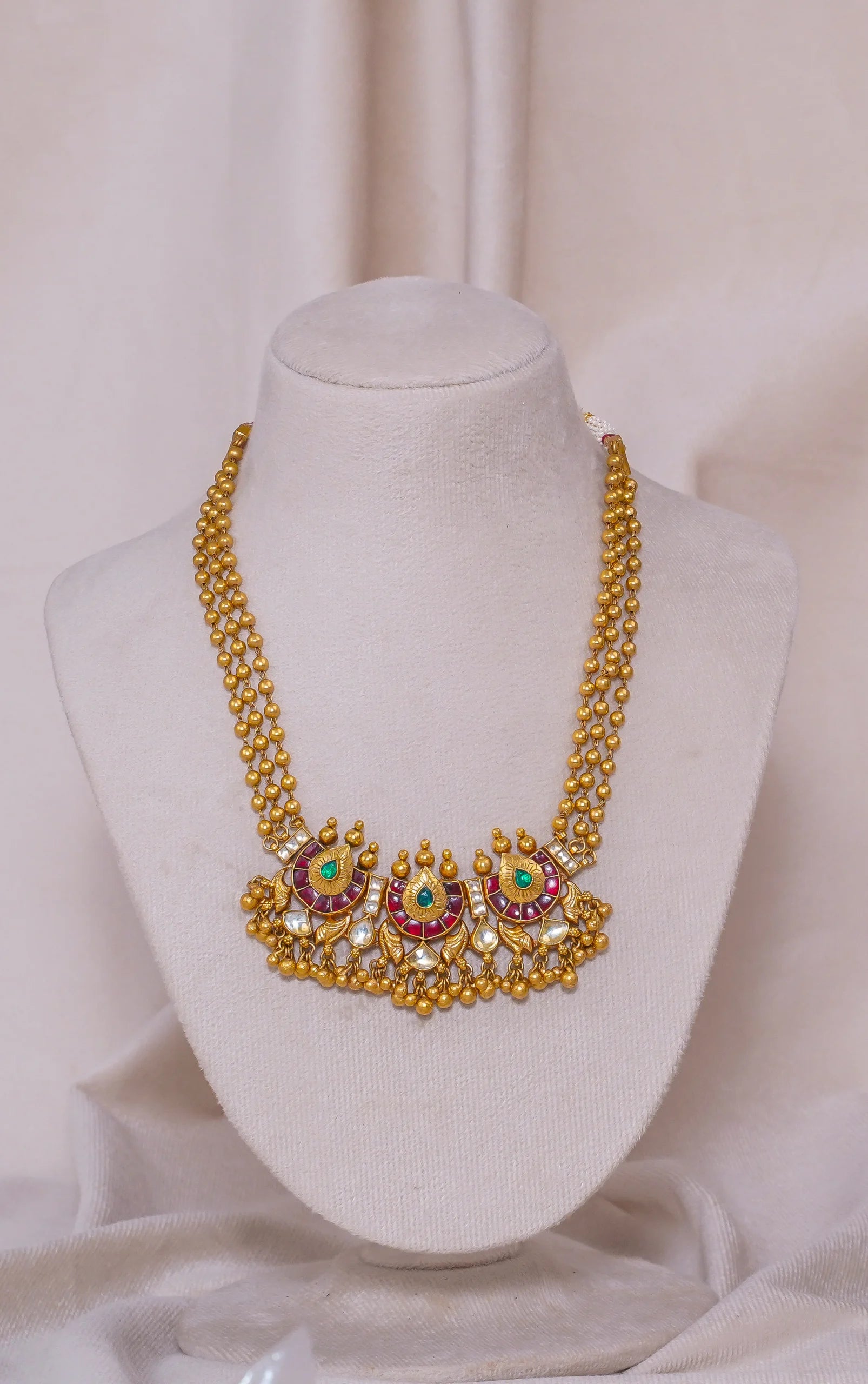 Elegant gold necklace with emerald and ruby accents, displayed on a mannequin.
