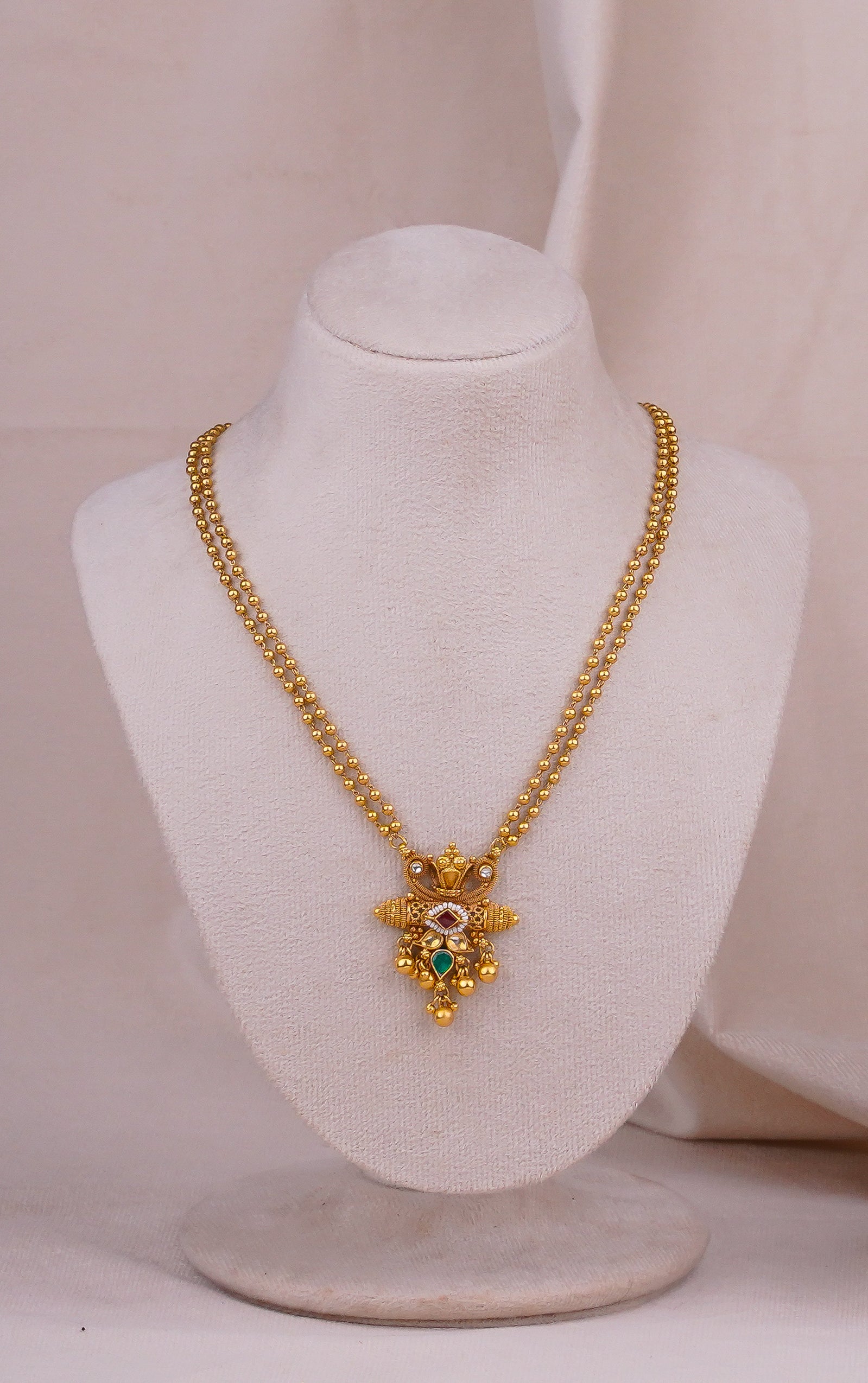Elegant gold necklace with intricate pendant and colorful gemstones displayed on mannequin