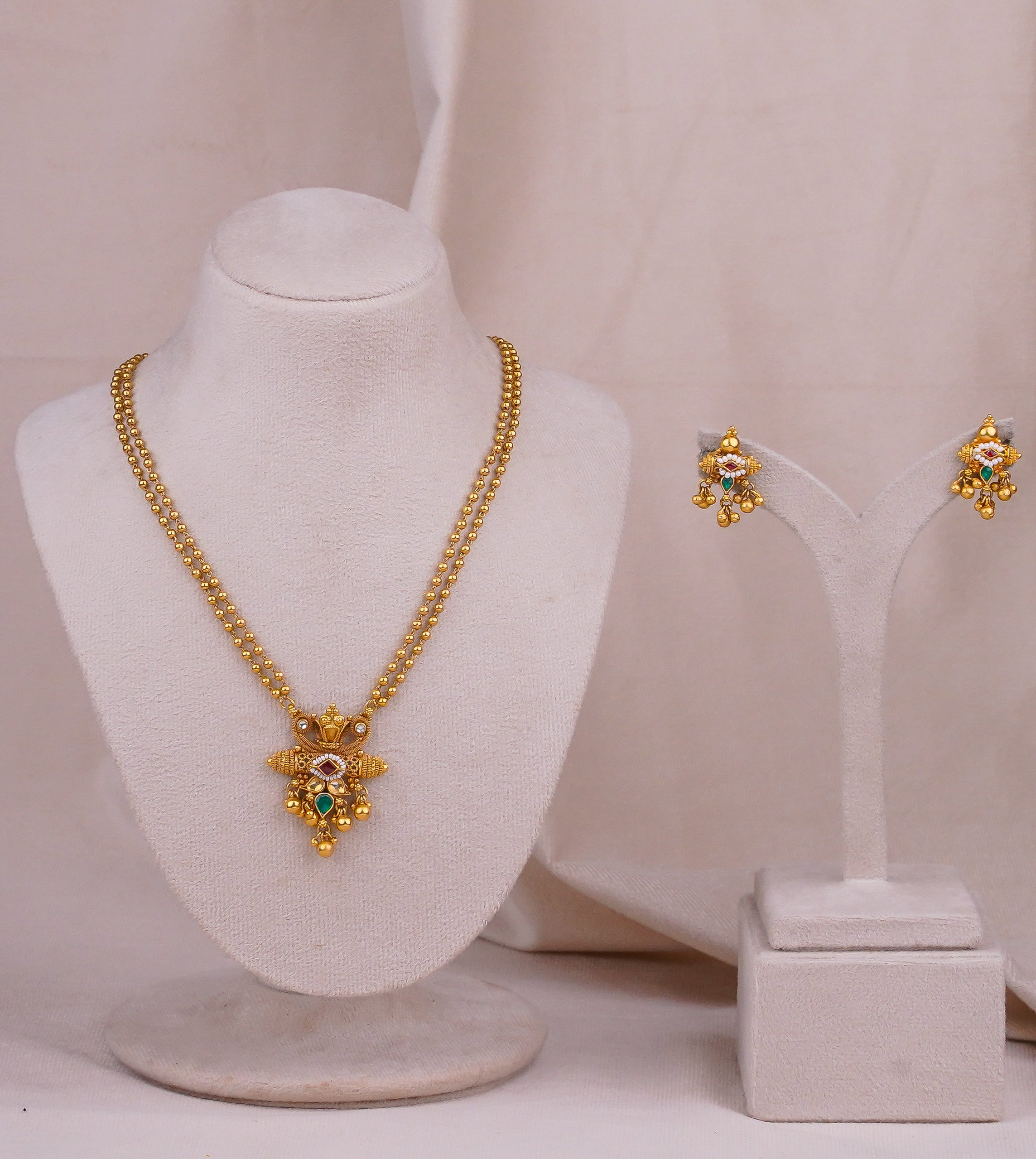 Traditional gold necklace set with emerald and ruby stones, paired with matching jhumka earrings for festive wear