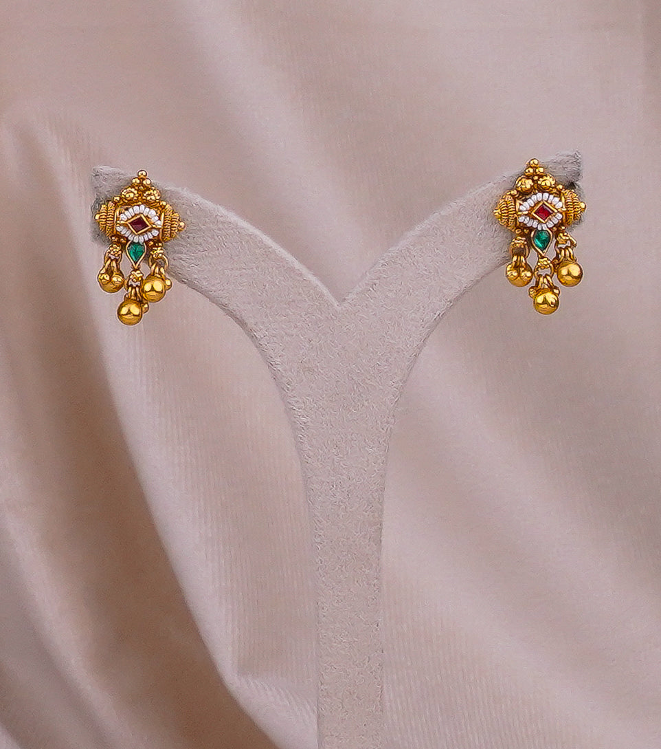 Gold earrings with red and green gemstones, intricate design, displayed on velvet
