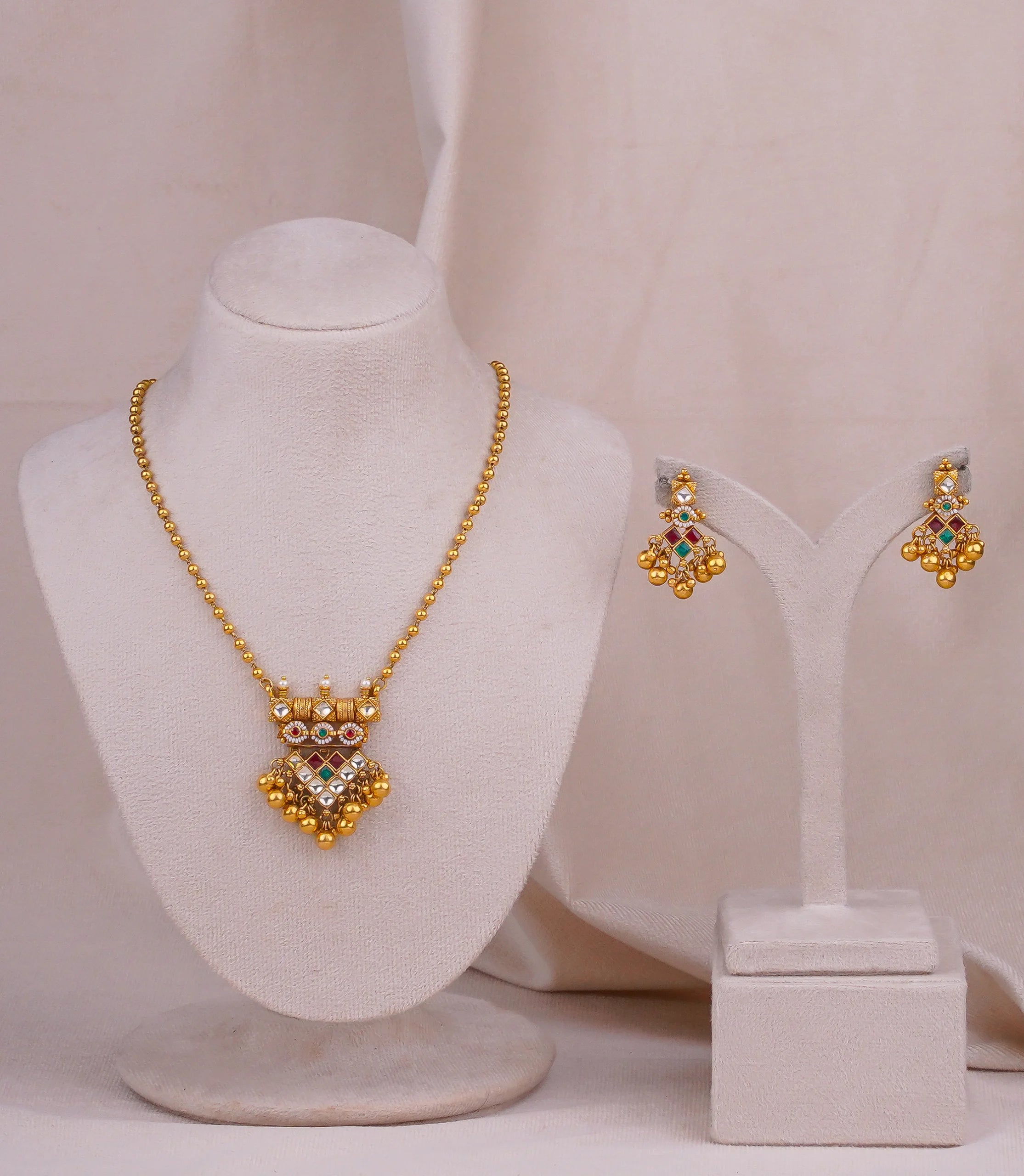Elegant gold necklace and matching earrings with colorful gemstones, displayed on mannequin busts.