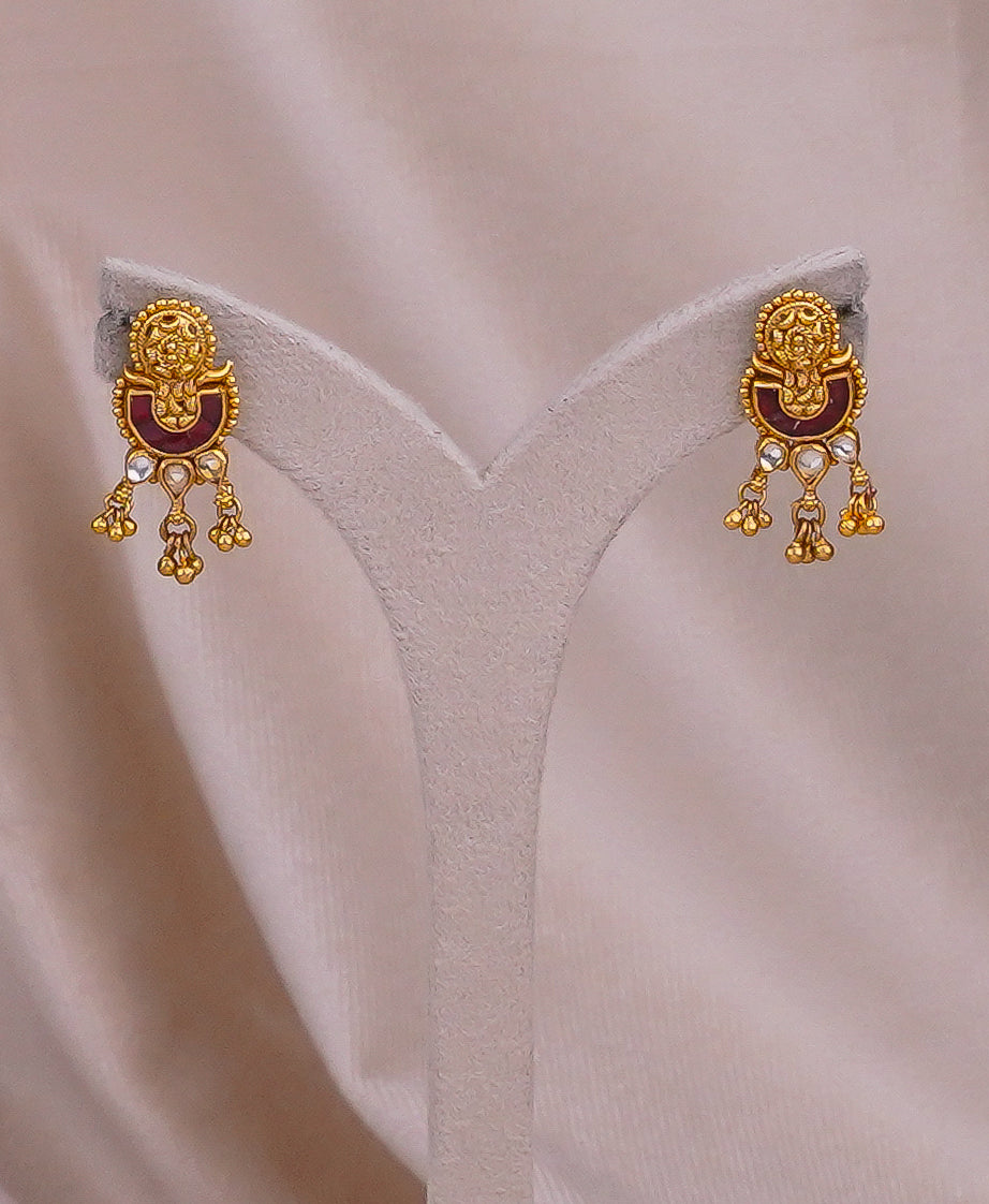 Gold-plated traditional jhumka earrings with red enamel and stone accents on display stand