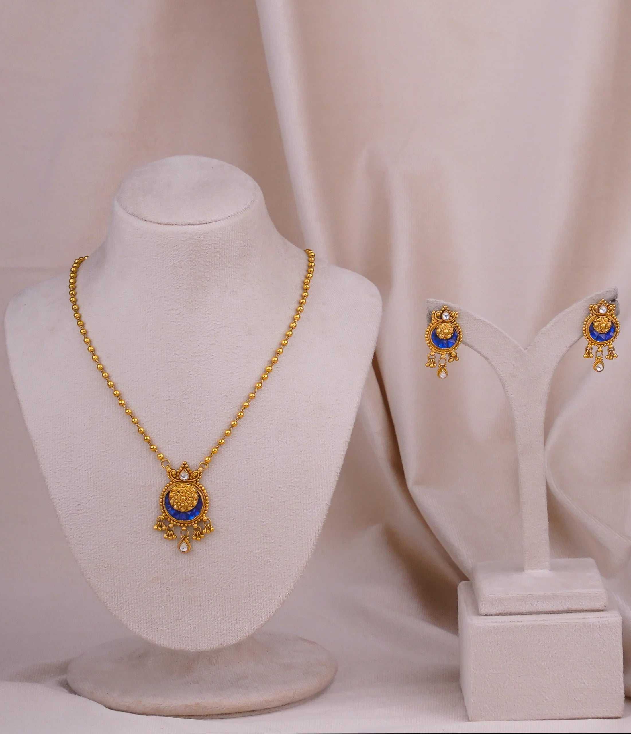Elegant gold necklace and matching earrings with blue gemstone pendant, displayed on mannequin for traditional jewelry collection
