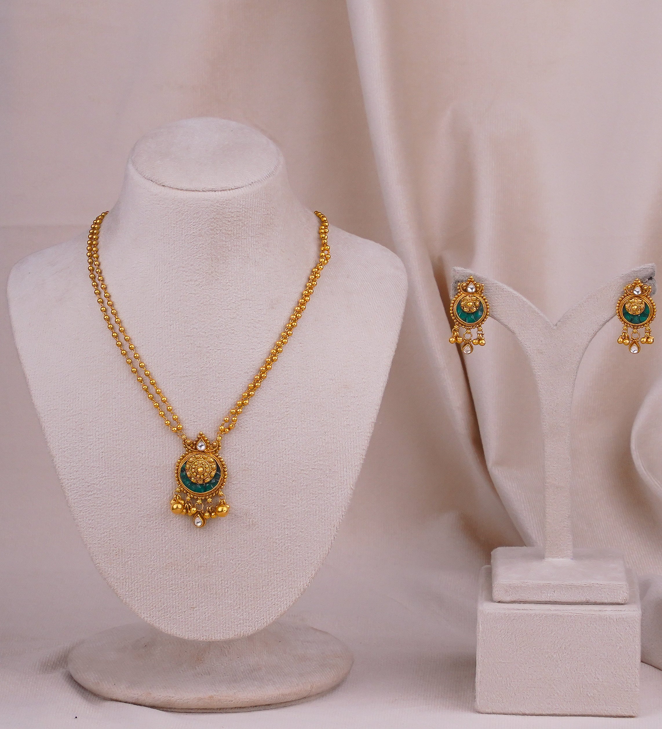 Gold necklace and earrings set with green stone and dangling beads, displayed on mannequins