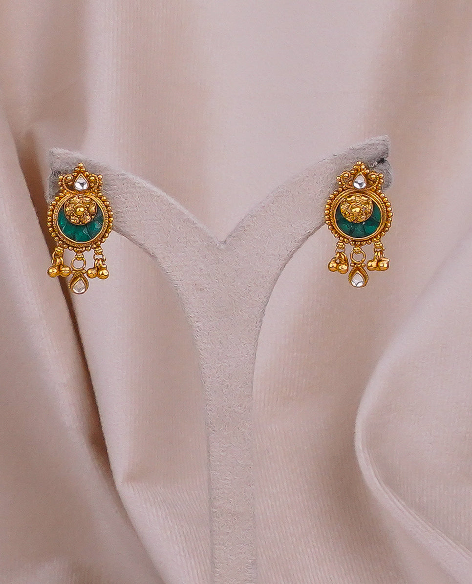 Gold jhumka earrings with green gemstone and dangling beads on velvet display