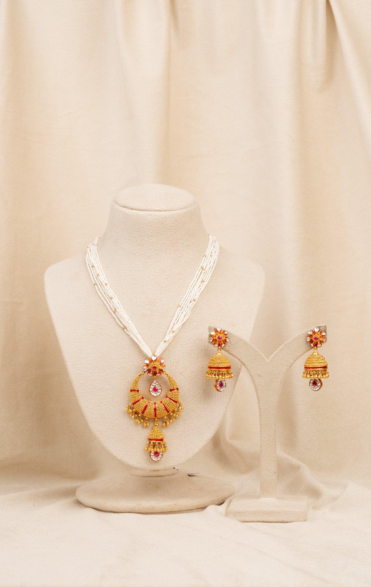 Elegant gold and red traditional necklace set with matching jhumka earrings, displayed on mannequin