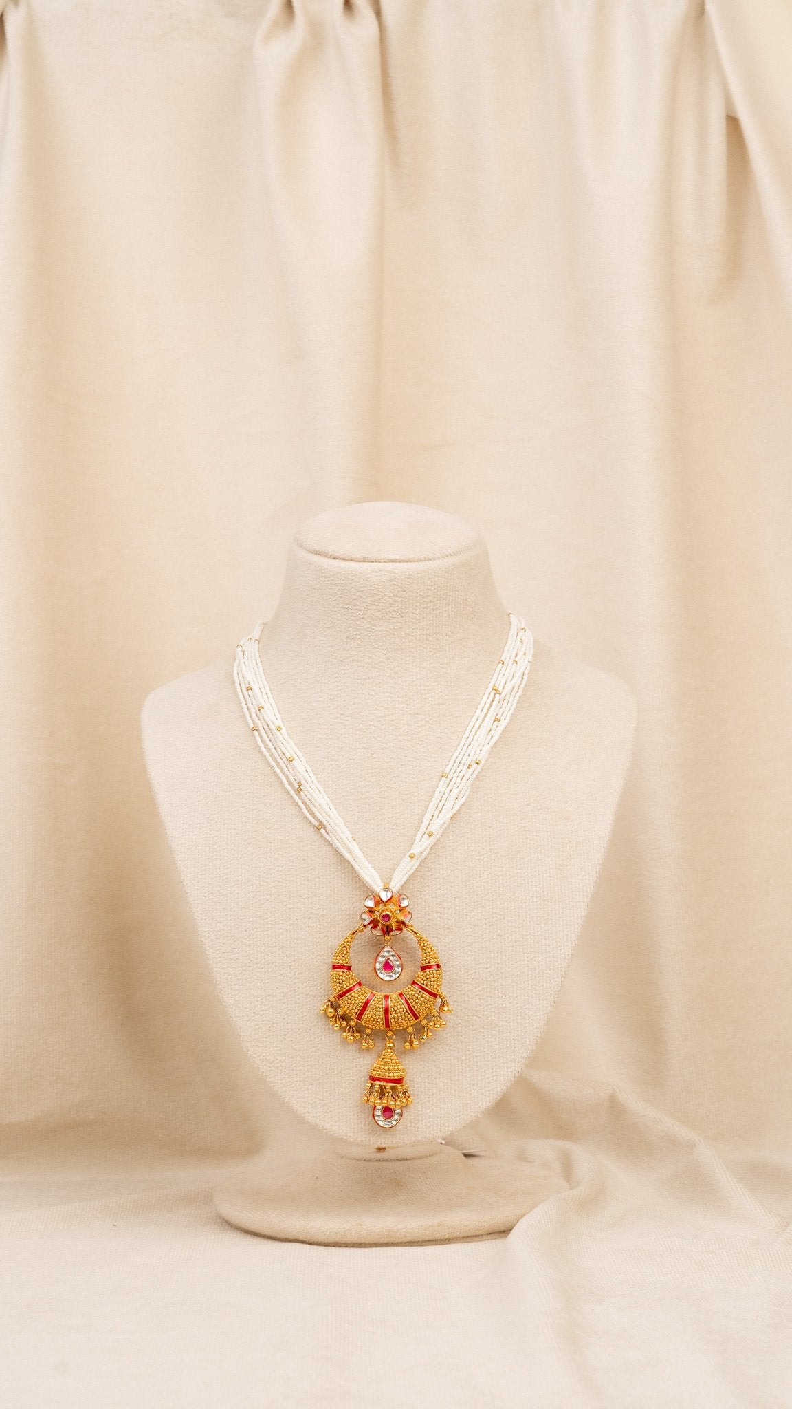 Elegant gold and white beaded necklace with red accents and dangling pendant, displayed on mannequin.
