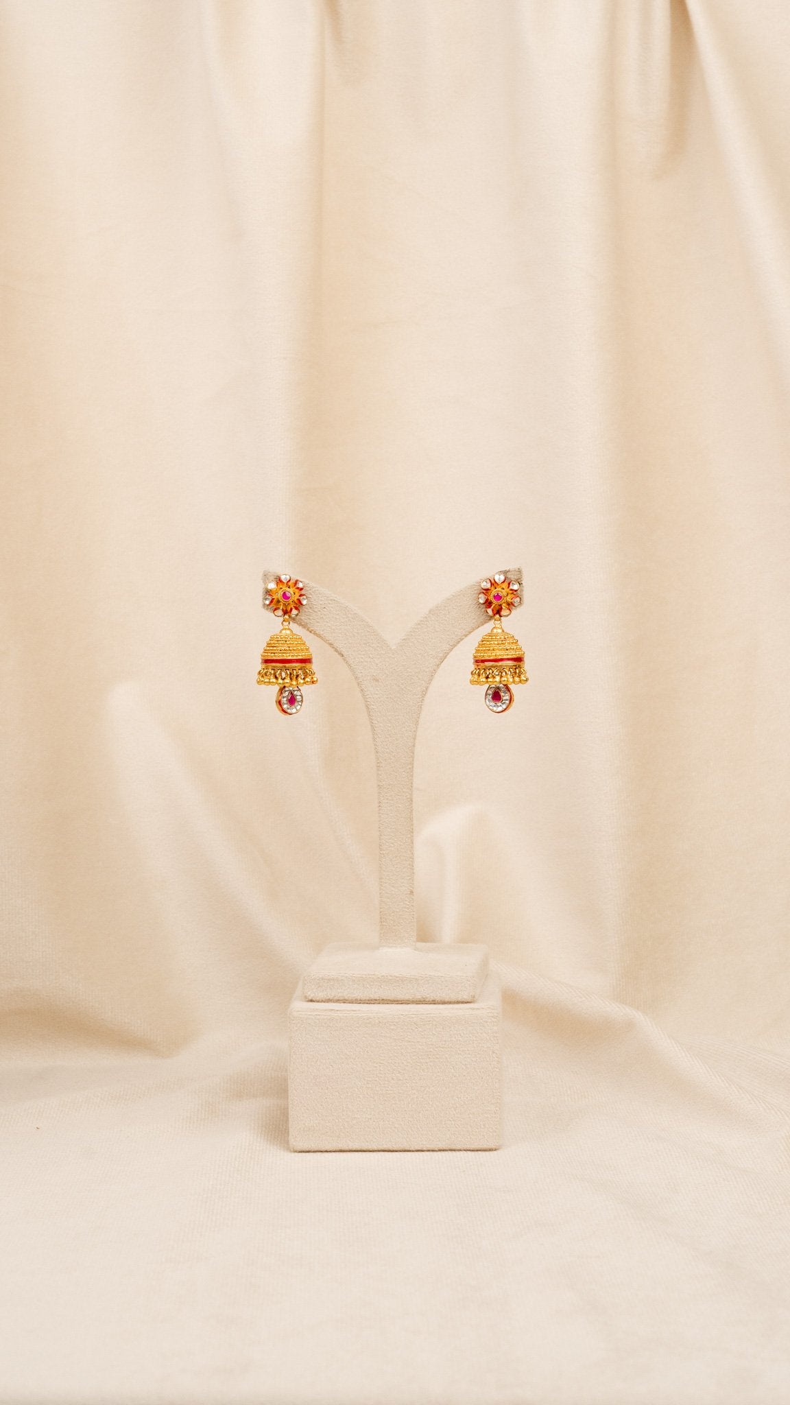 Gold jhumka earrings with red and white stones on display stand