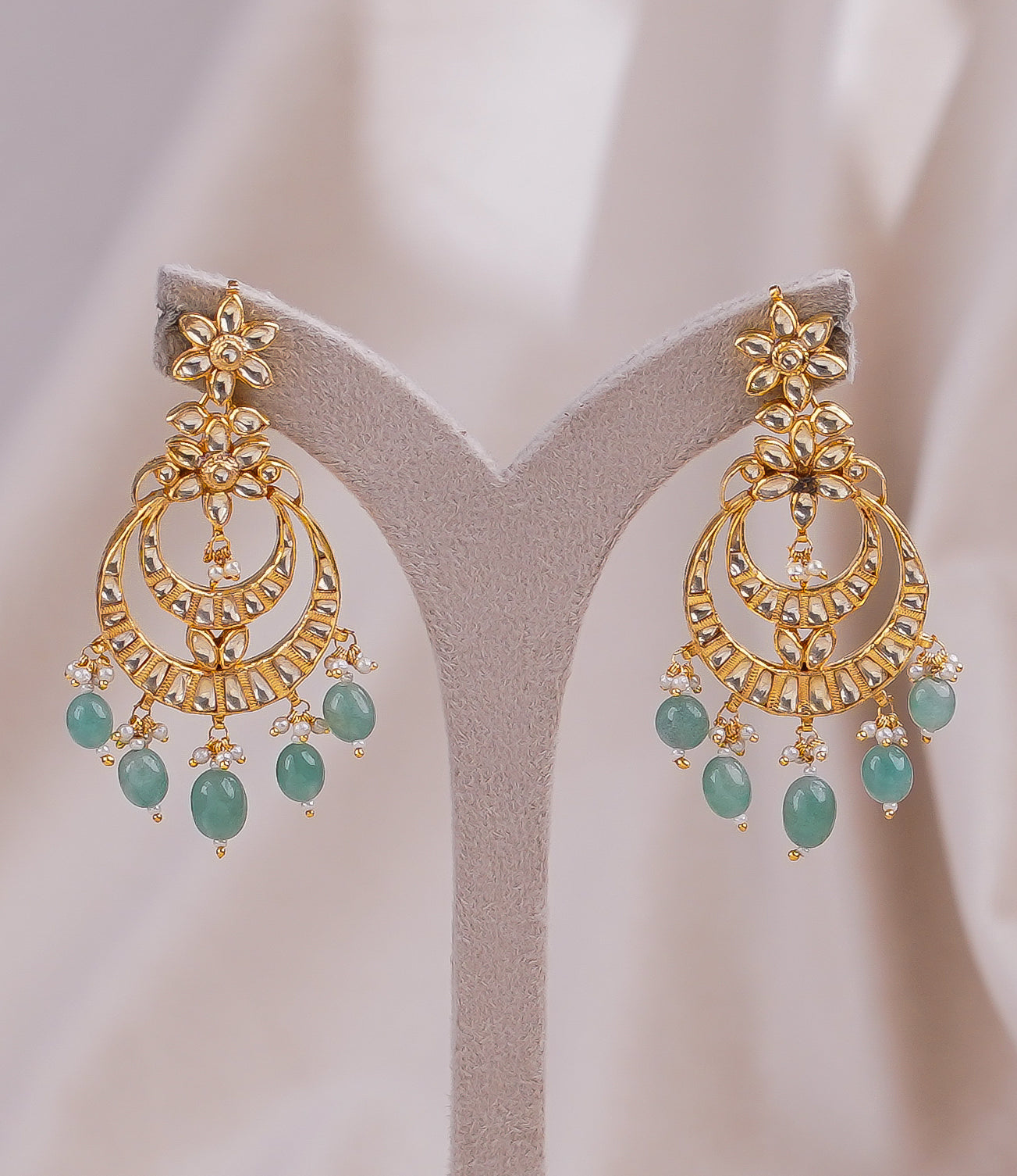 Gold floral chandelier earrings with green gemstones and pearl accents, displayed on stand