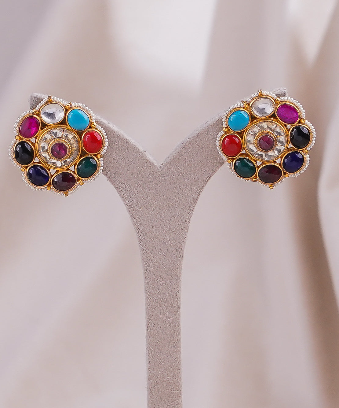 Colorful gemstone stud earrings with gold-tone setting and pearl accents, displayed on stand