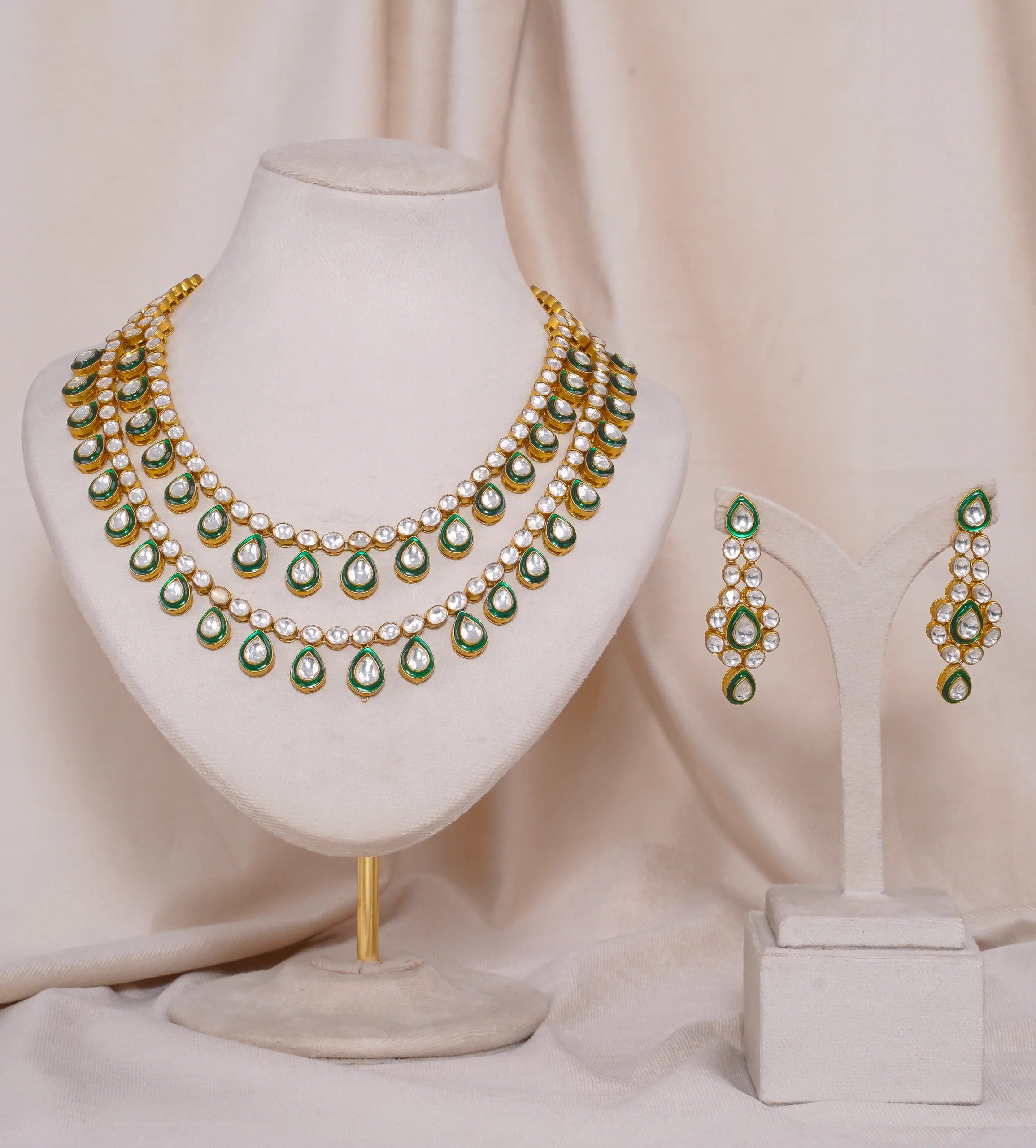 Gold kundan necklace and earrings set with green enamel and white stones, displayed on mannequin