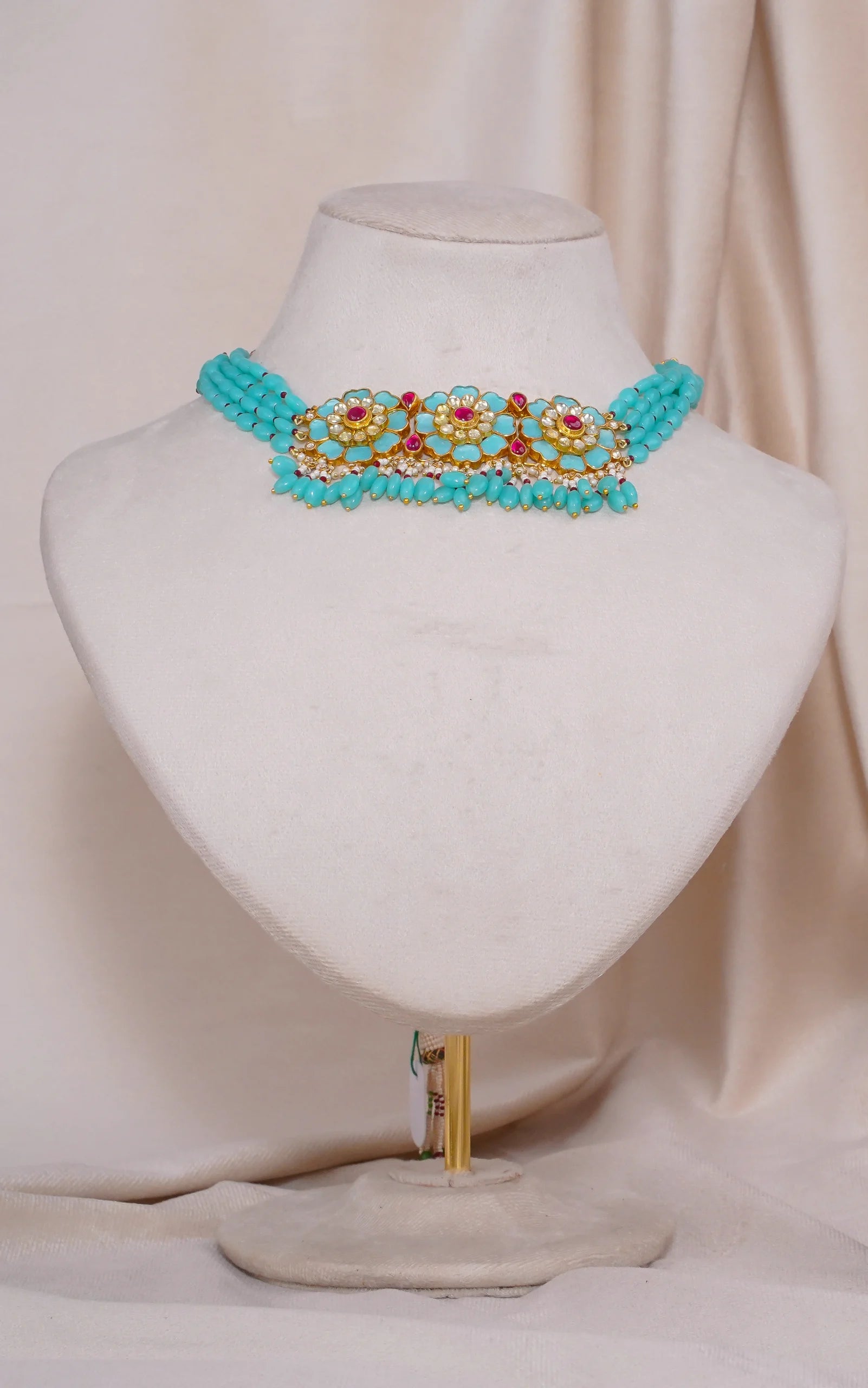Turquoise beaded choker necklace with gold floral design and red gem accents, displayed on mannequin