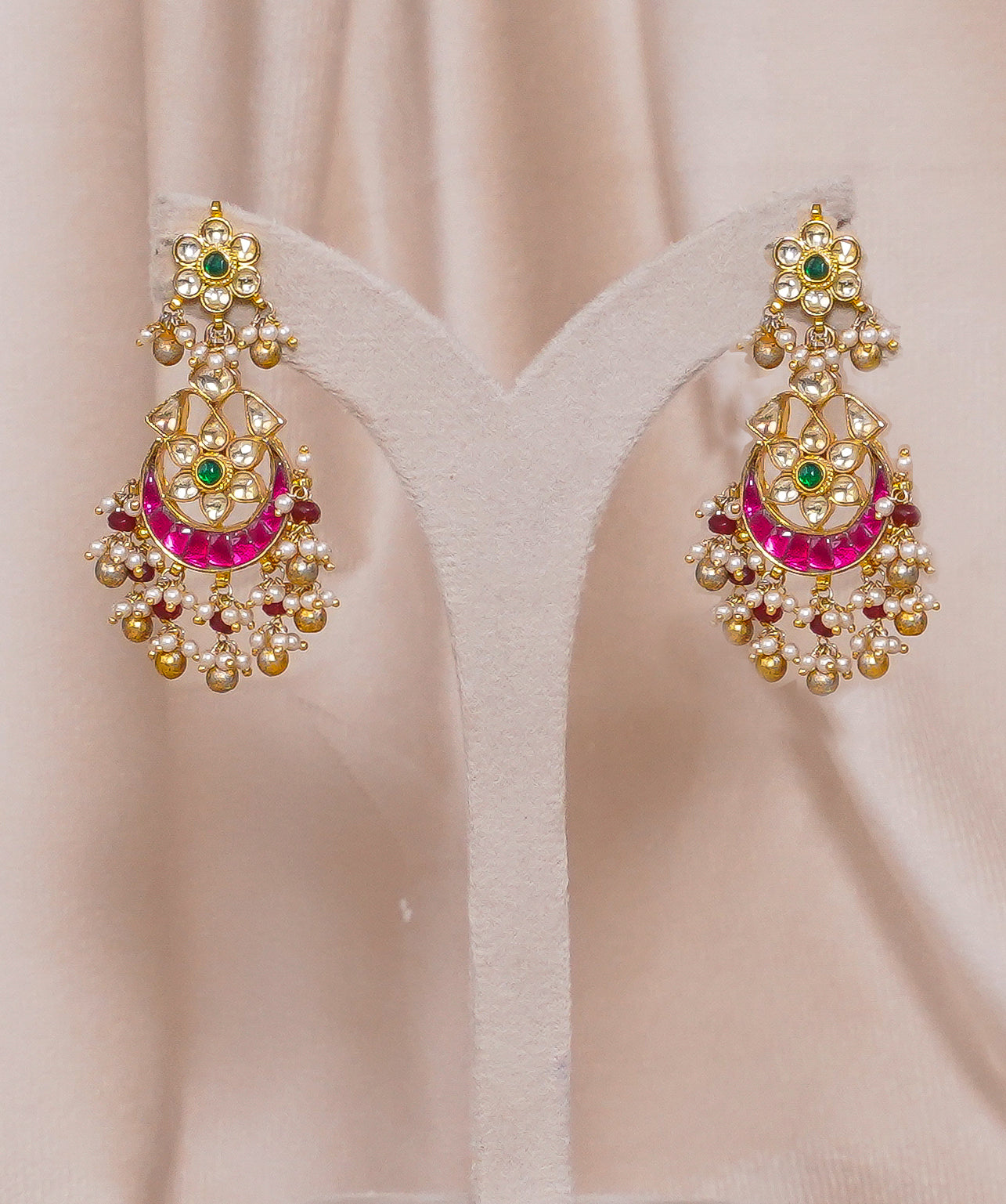 Gold jhumka earrings with pink enamel, green stones, and pearl drops for traditional wear
