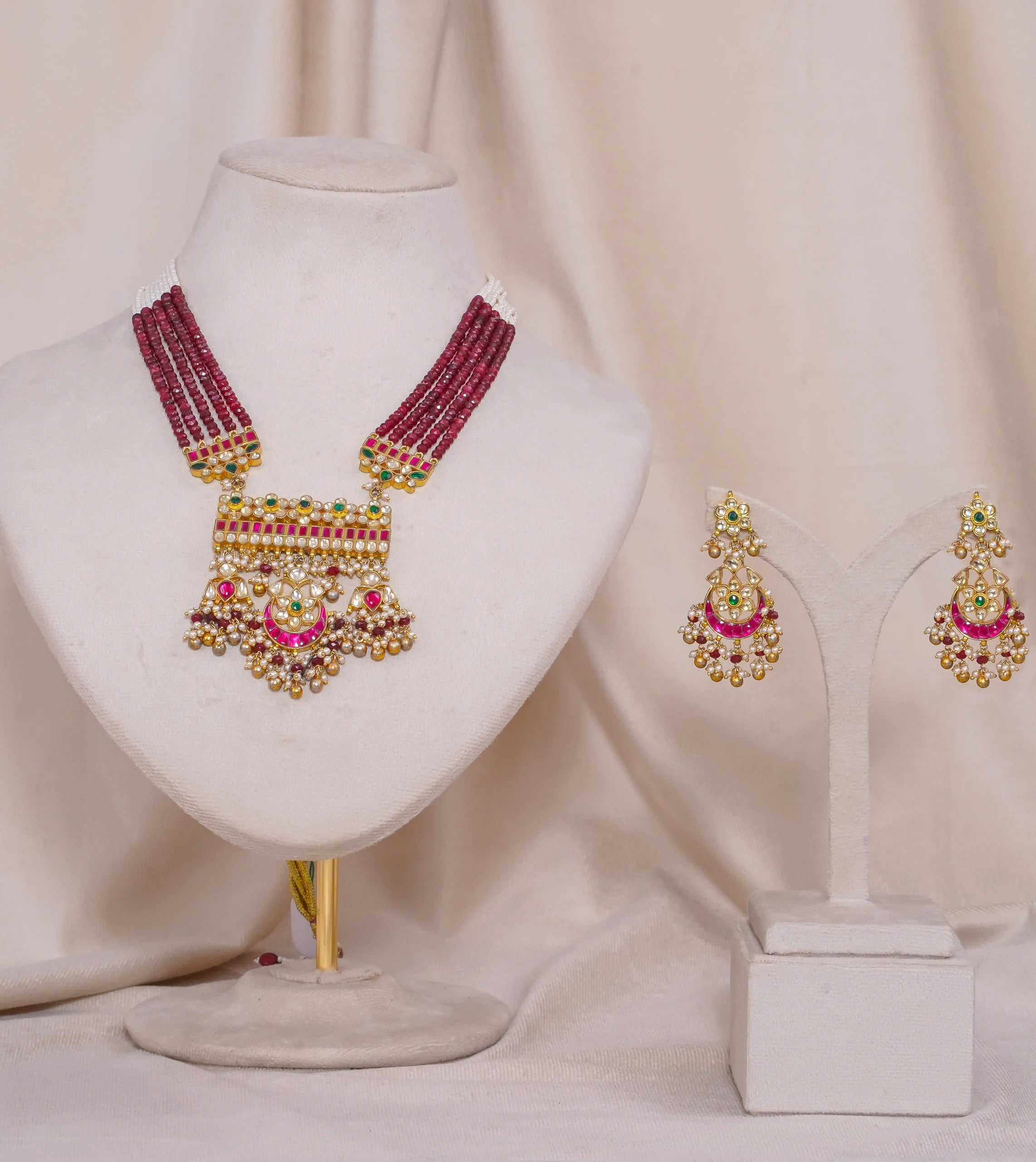 Traditional Indian gold necklace set with red beads, pearls, and green accents, paired with matching earrings.
