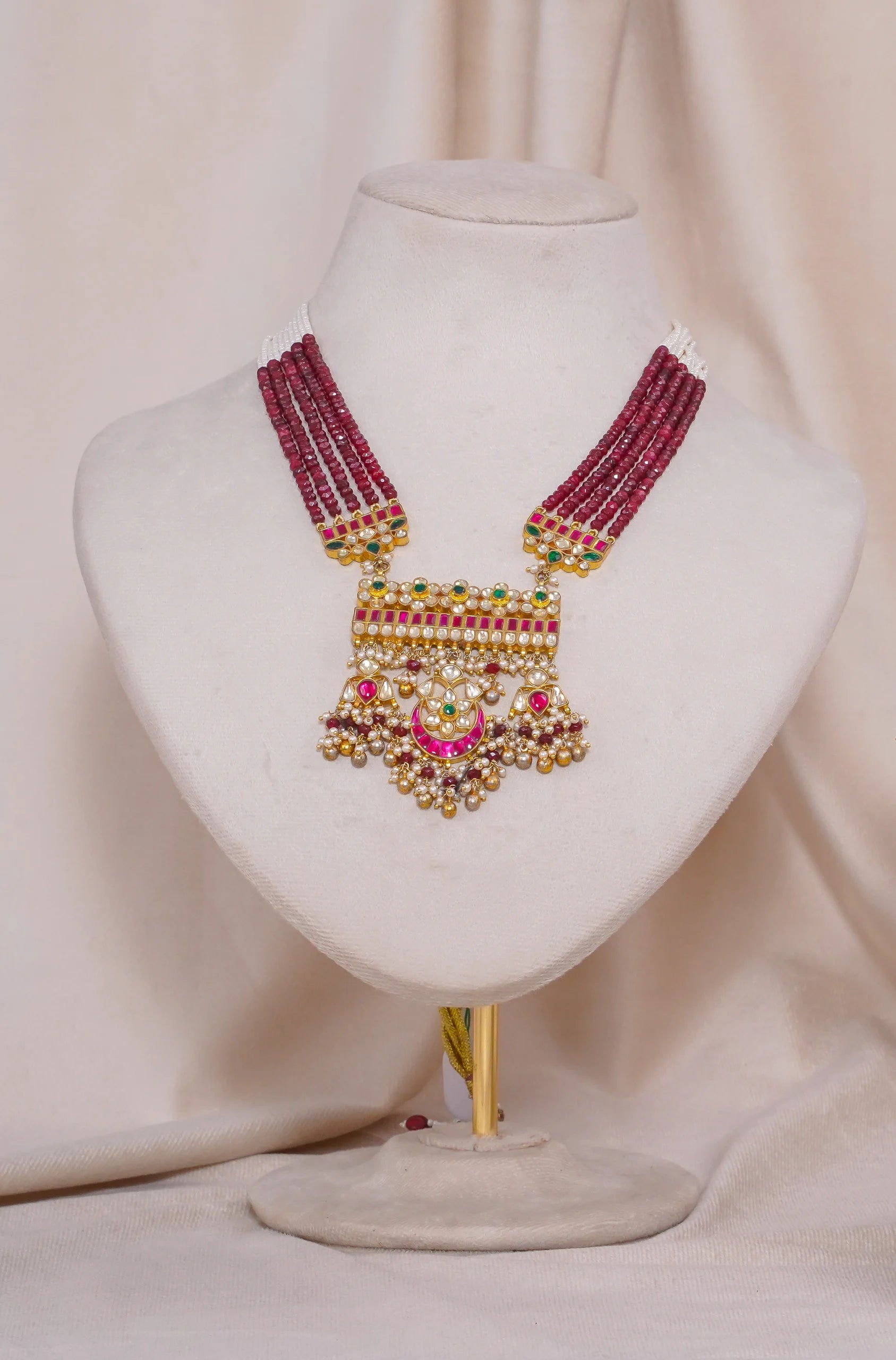 Traditional Indian necklace with red beads, pearls, and gold pendant, displayed on mannequin