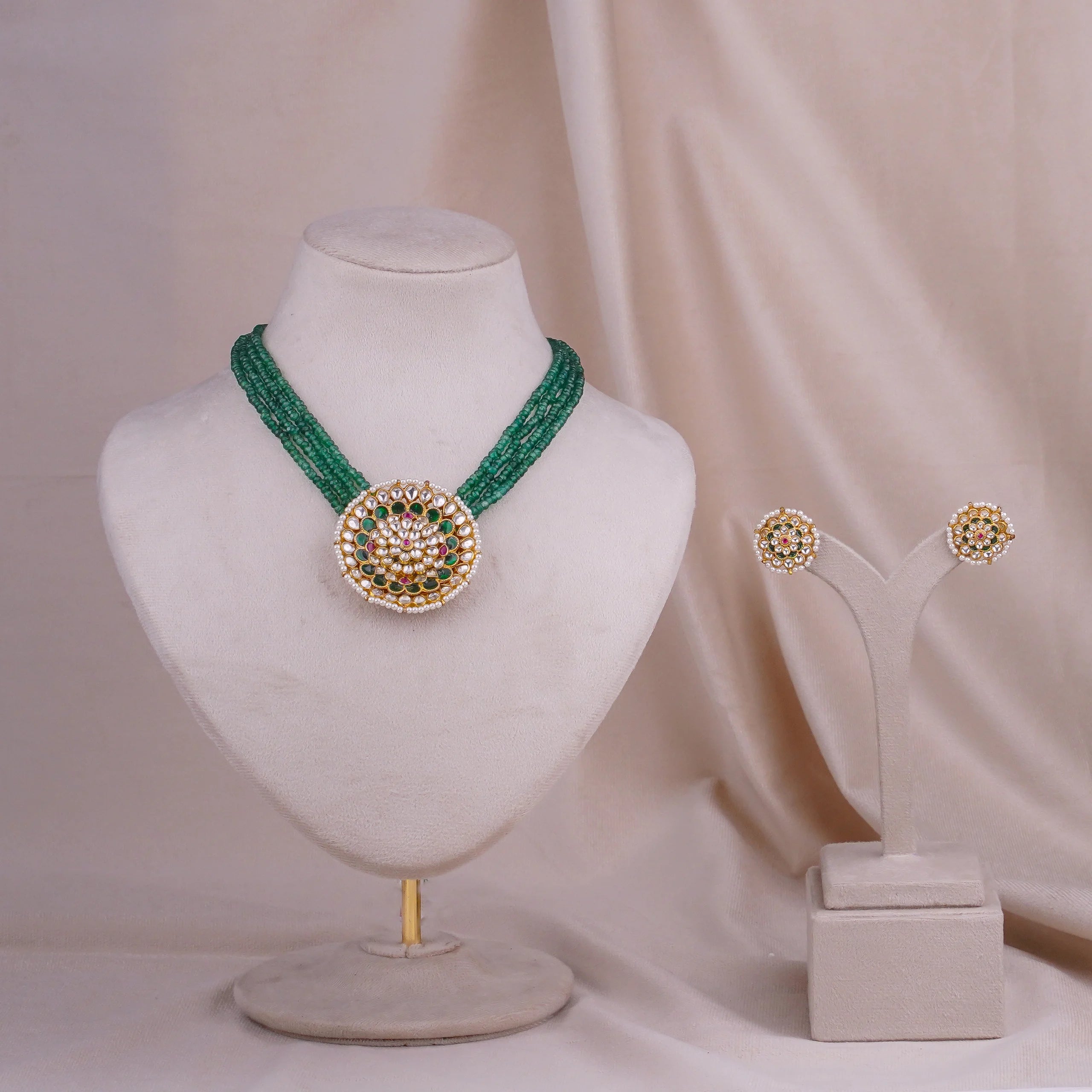 Emerald beaded necklace with gold kundan pendant and matching stud earrings on display stands