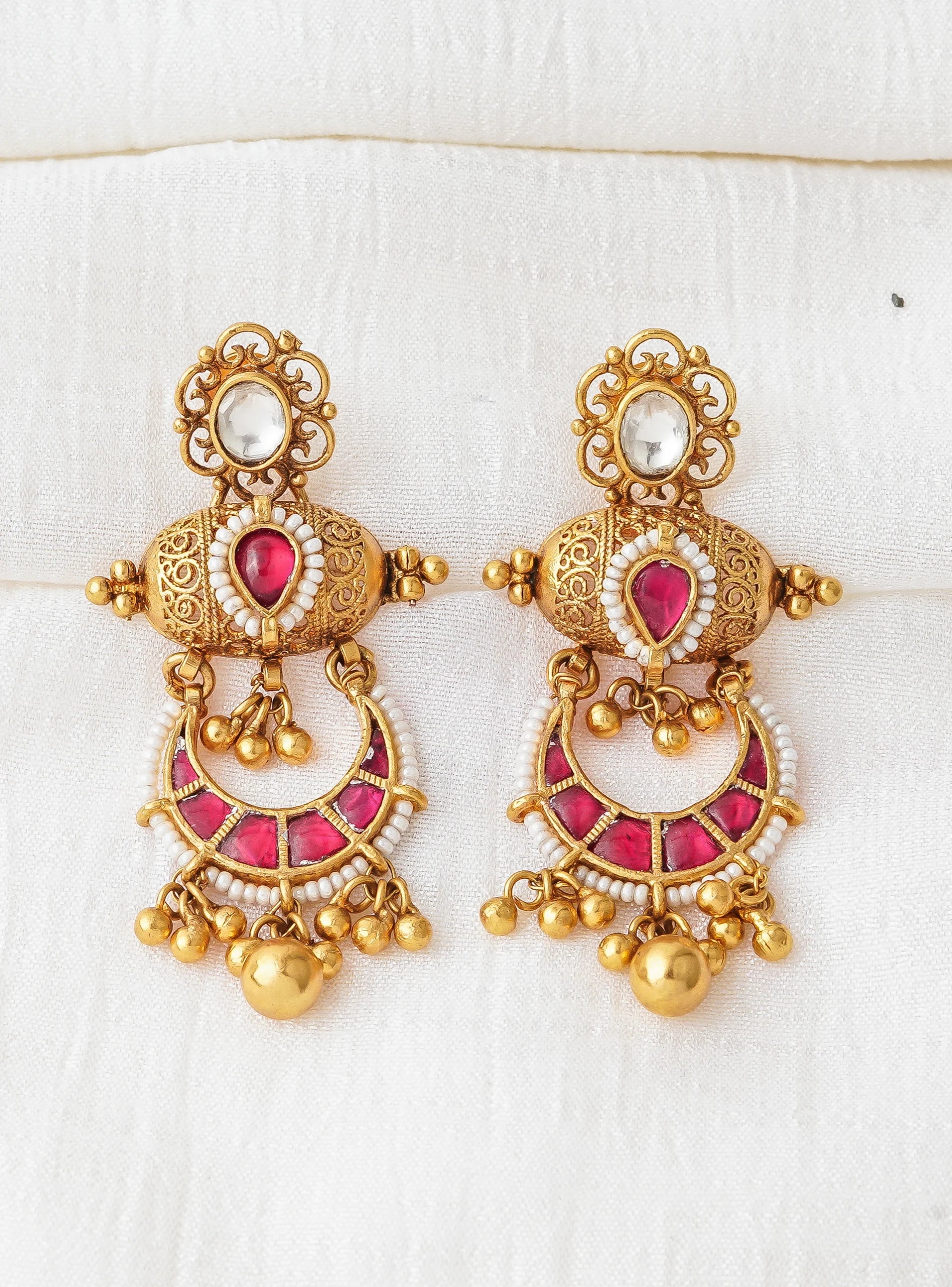 Gold jhumka earrings with red gemstones and white beads, traditional Indian jewelry design