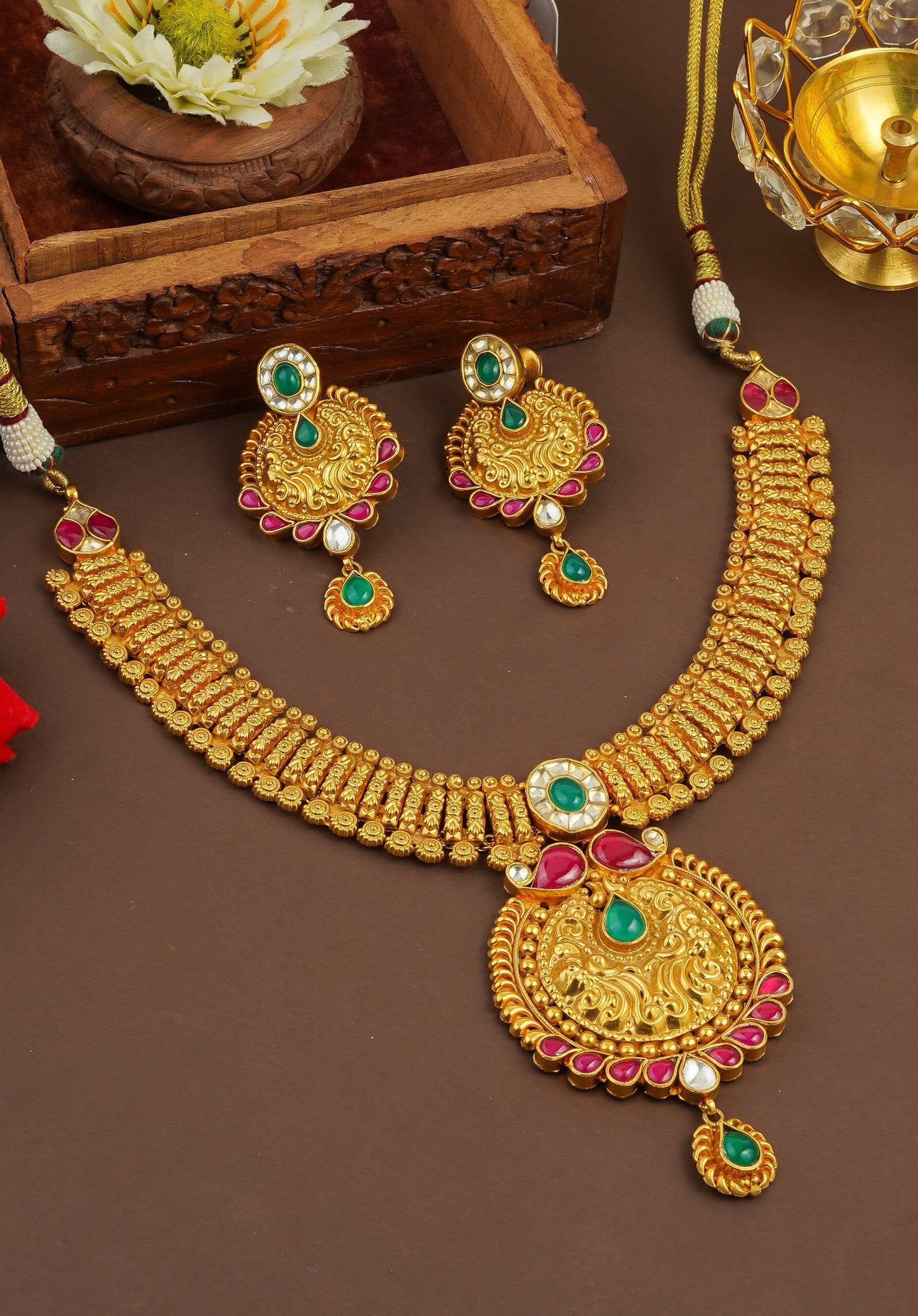 Elegant gold necklace and earrings set with green and pink gemstones, displayed on a wooden tray.