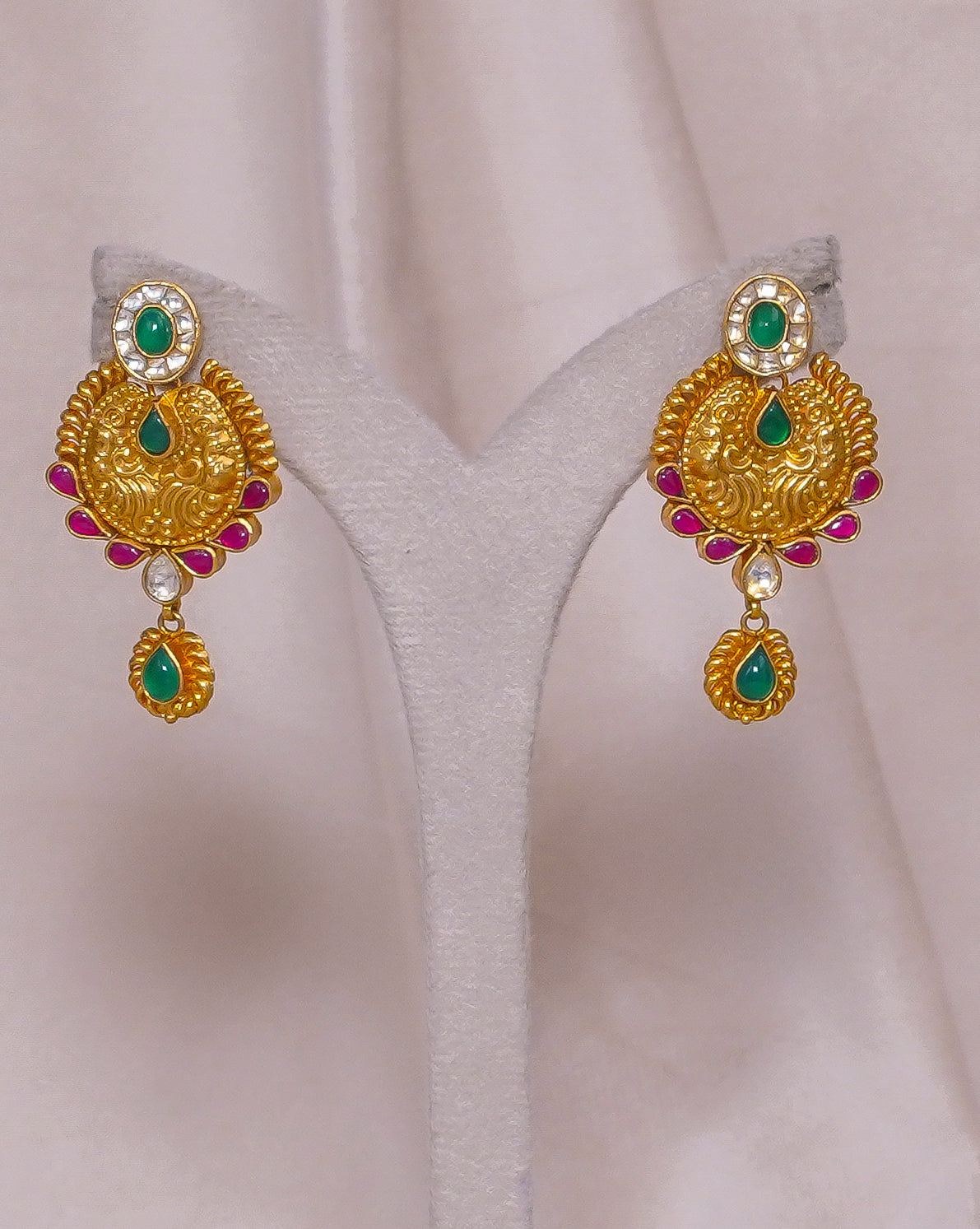 Gold earrings with emerald, ruby, and diamond accents, displayed on a white stand