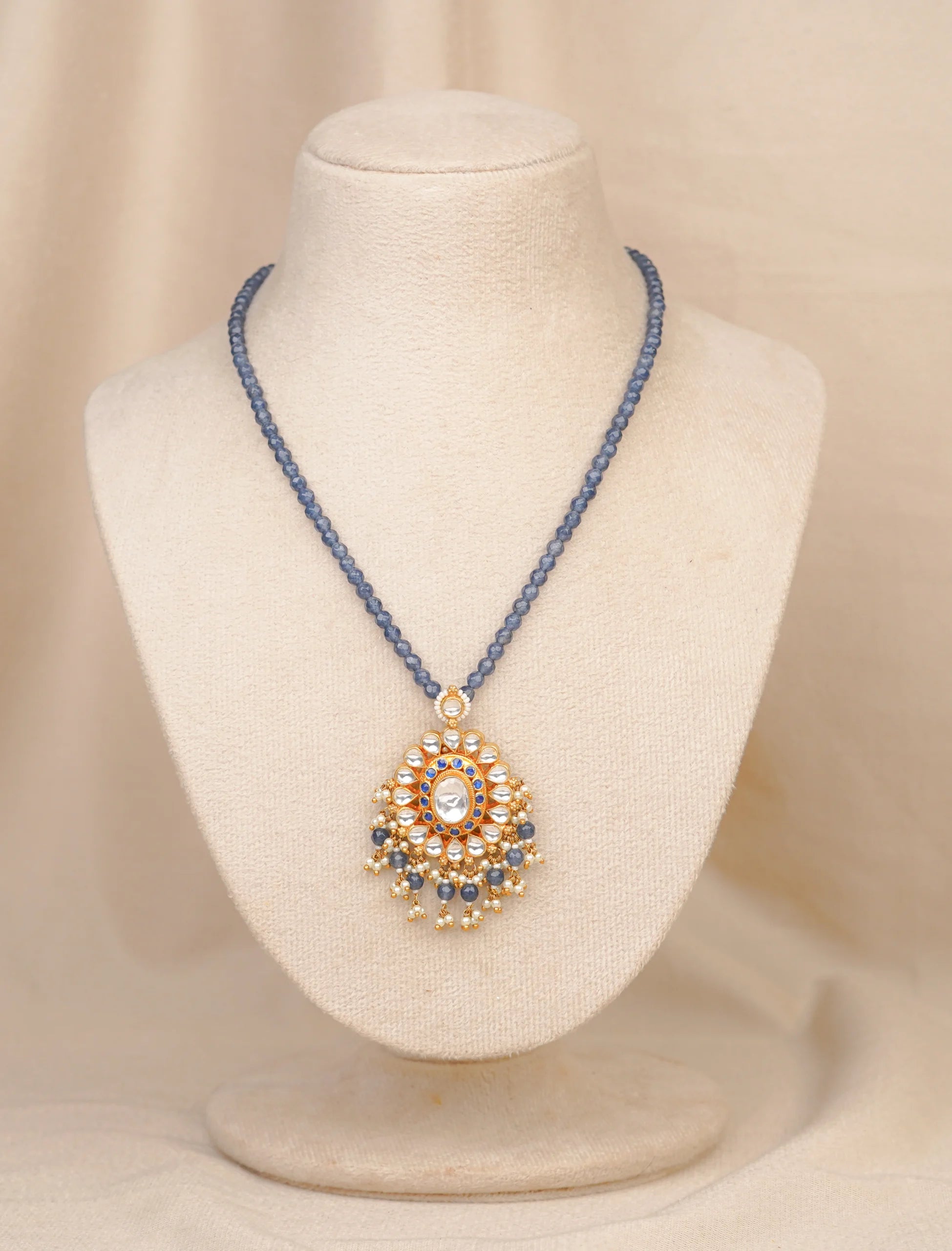 Elegant blue beaded necklace with gold pendant, featuring kundan and pearl details, displayed on mannequin.