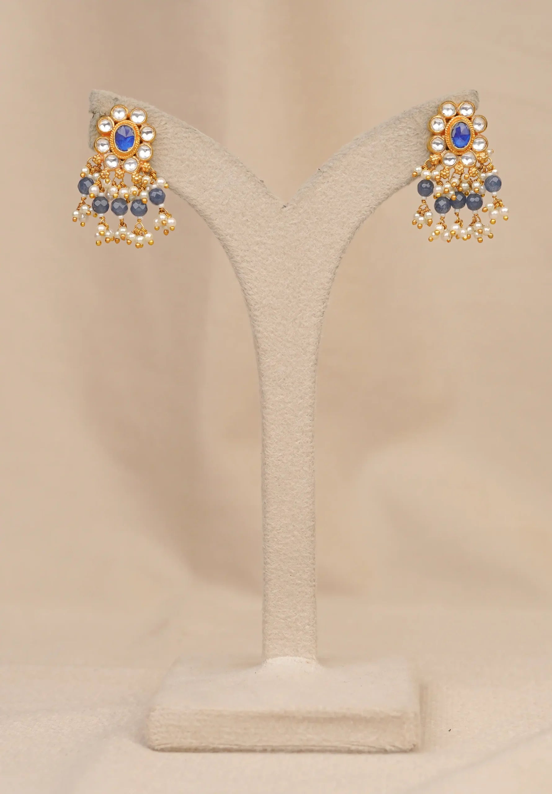 Gold earrings with blue gemstones and pearl drops, displayed on a stand