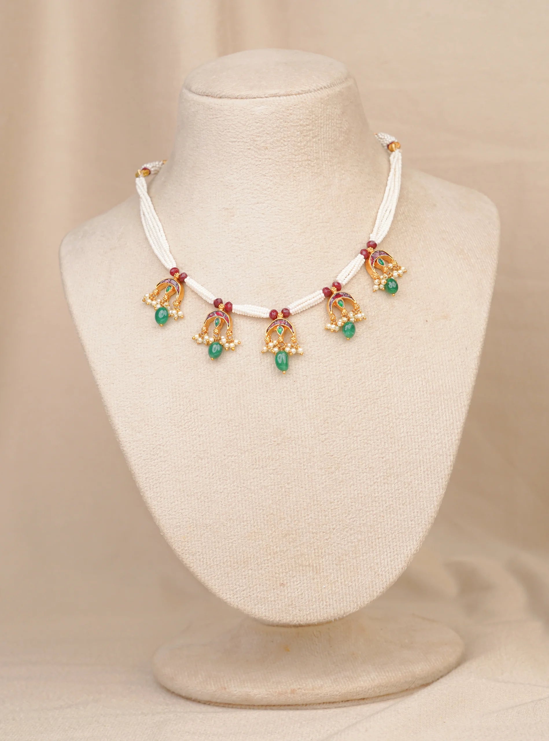Elegant gold necklace with green gemstones and pearl accents on a mannequin