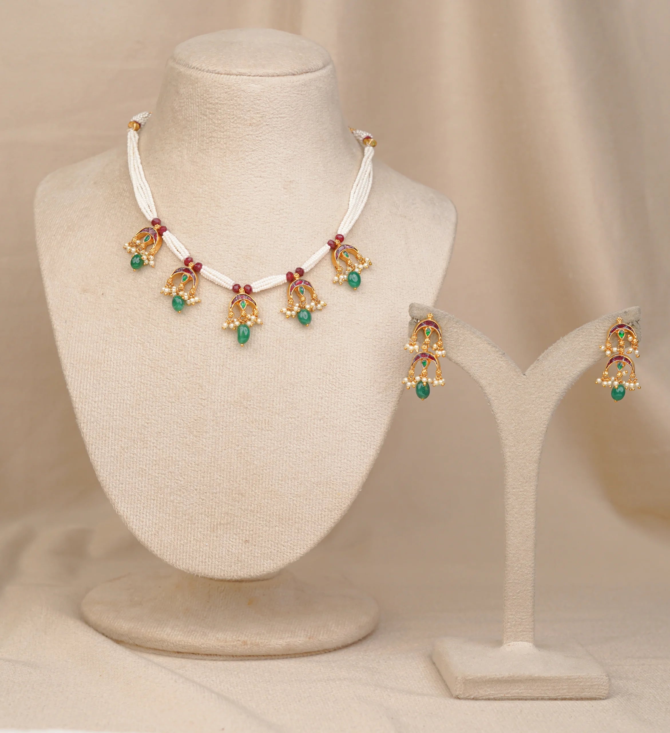 Elegant gold necklace and earrings set with green and red gemstones, displayed on mannequin stands.