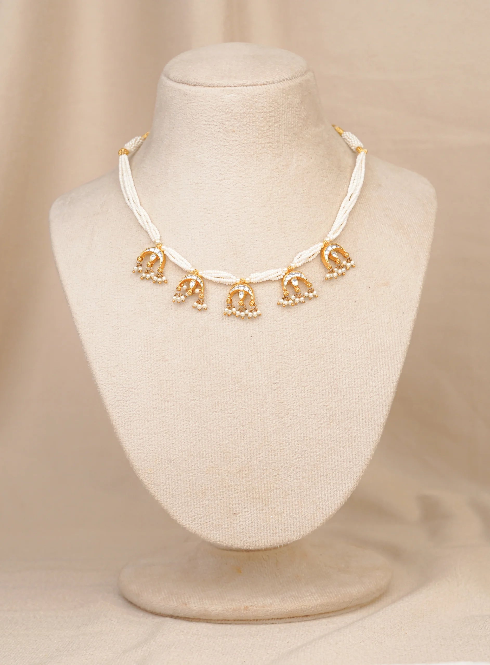 Elegant gold and white beaded choker necklace with dangling pearl and stone motifs, displayed on mannequin.