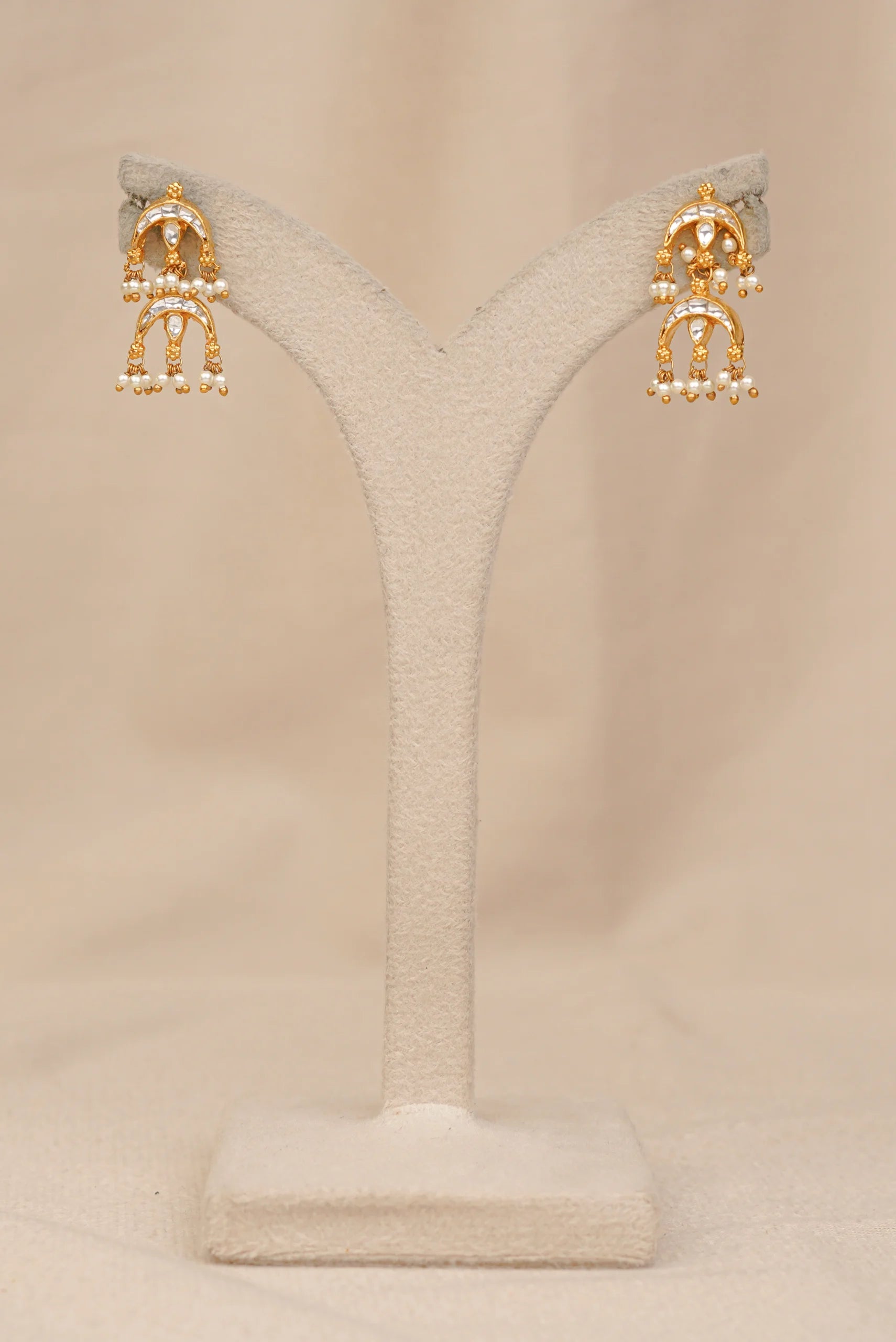 Elegant gold earrings with pearls and stones on a display stand