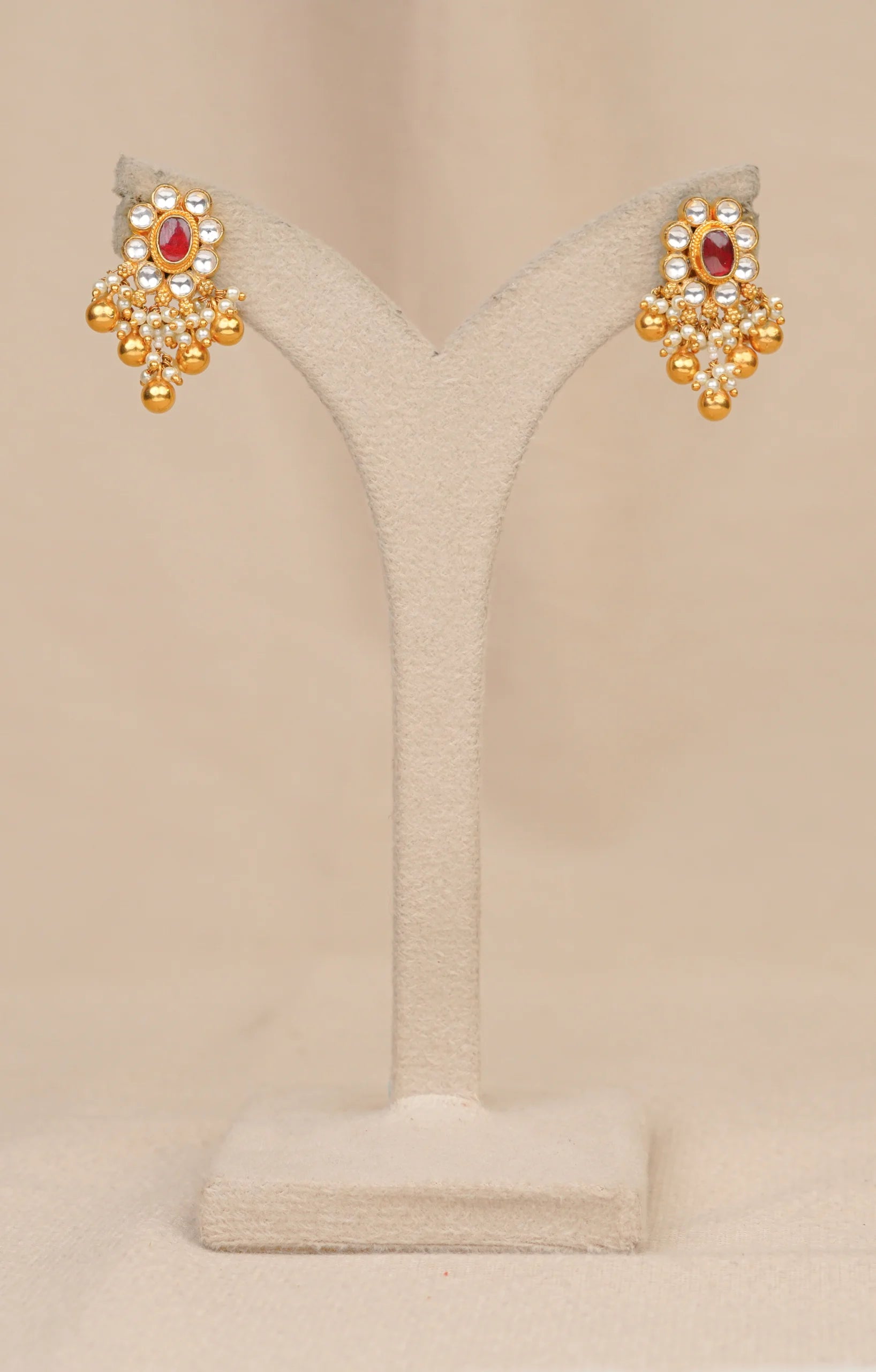 Gold earrings with red stone, pearls, and kundan detailing on display stand