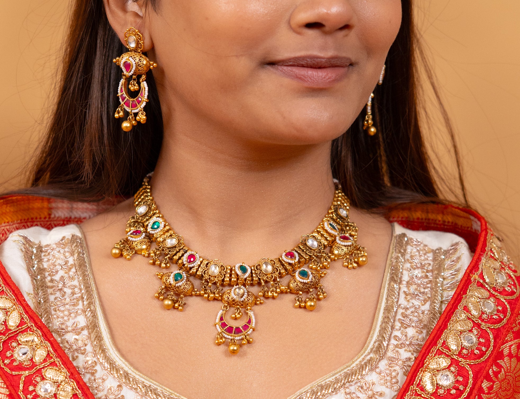 Elegant gold necklace and earrings set with red and green gemstones, perfect for traditional Indian weddings and festive occasions.