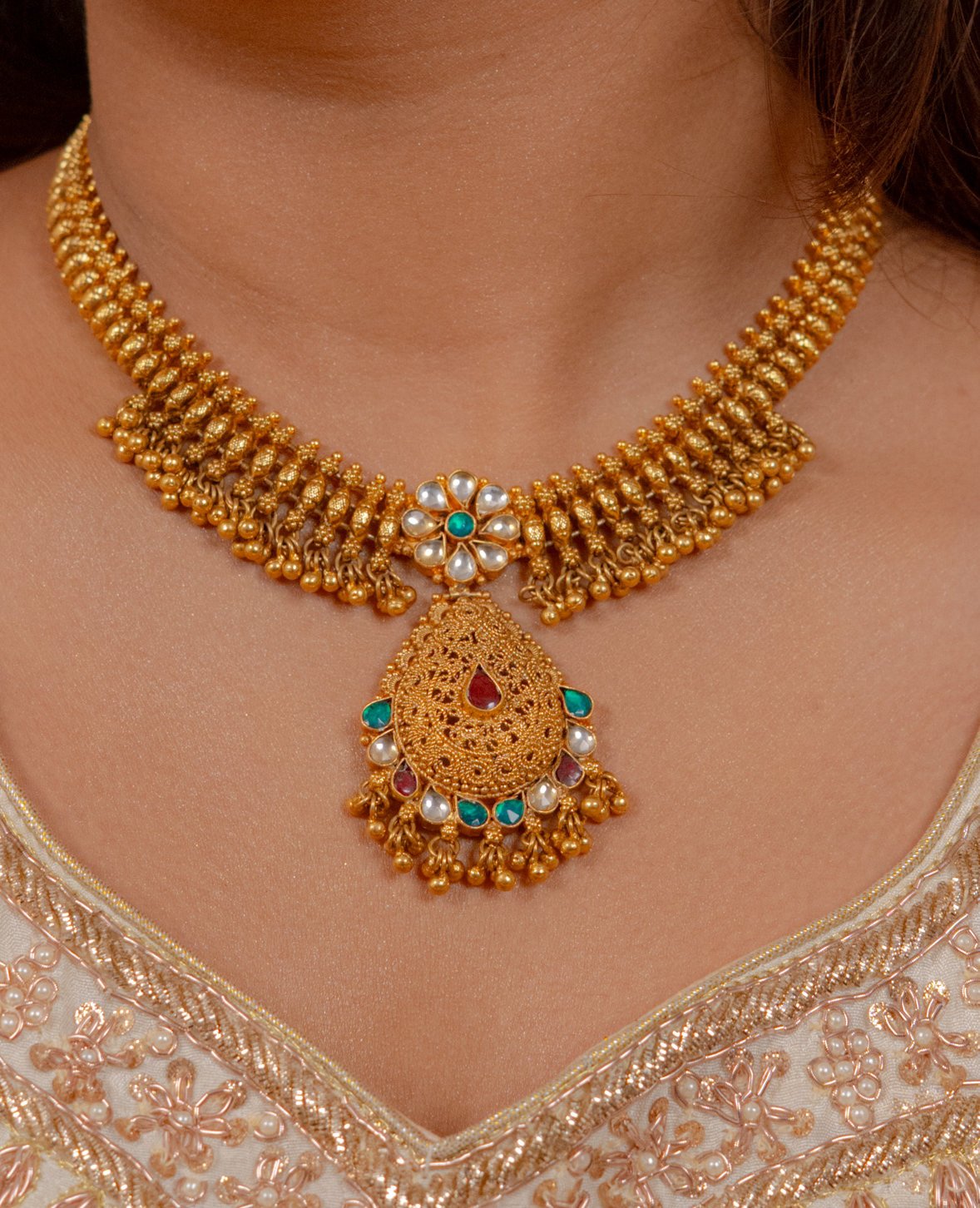 Elegant gold necklace with floral pendant, pearls, and gemstones, perfect for traditional wear.