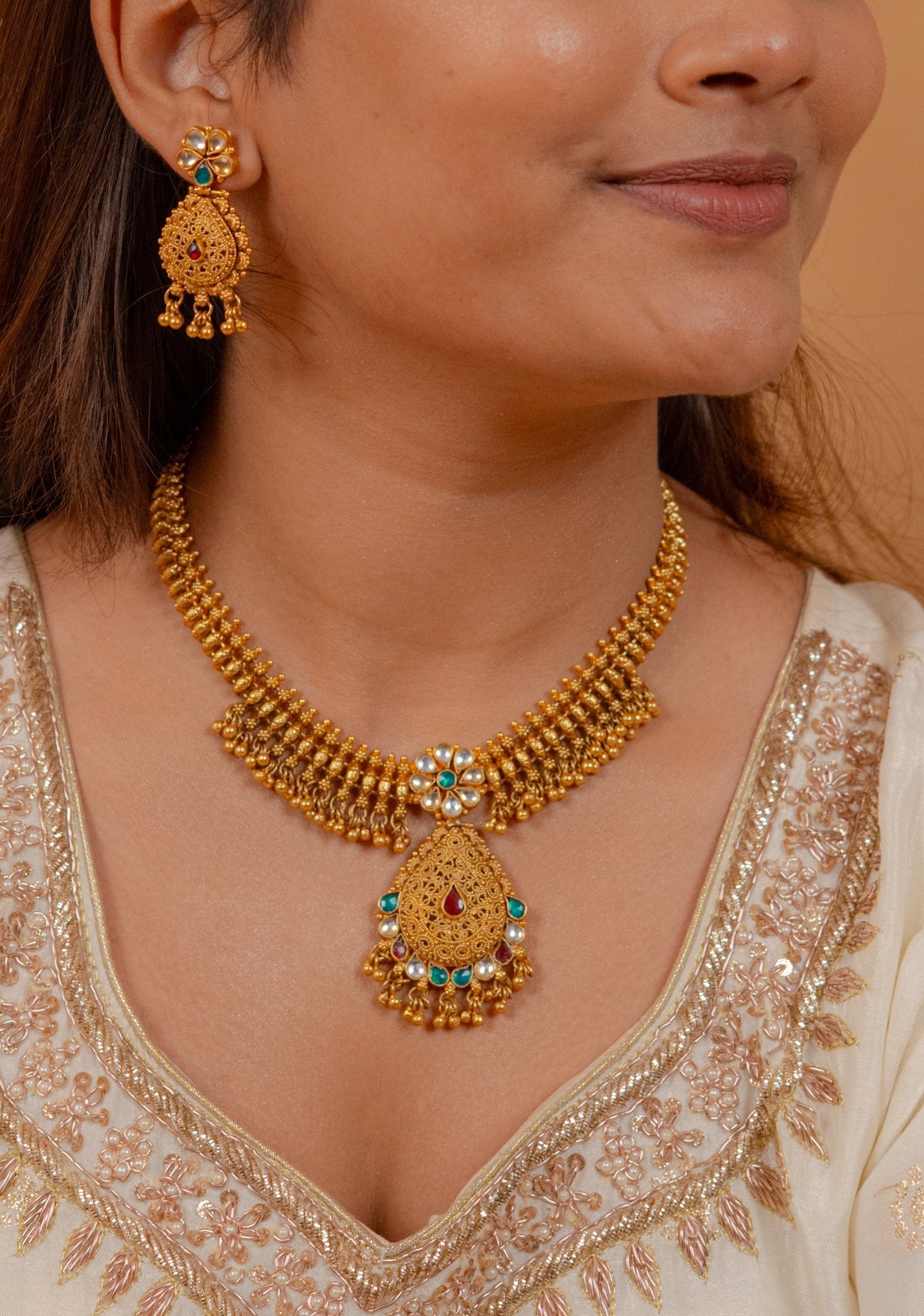 Elegant gold necklace and earrings set with gemstones and pearls, perfect for traditional occasions.