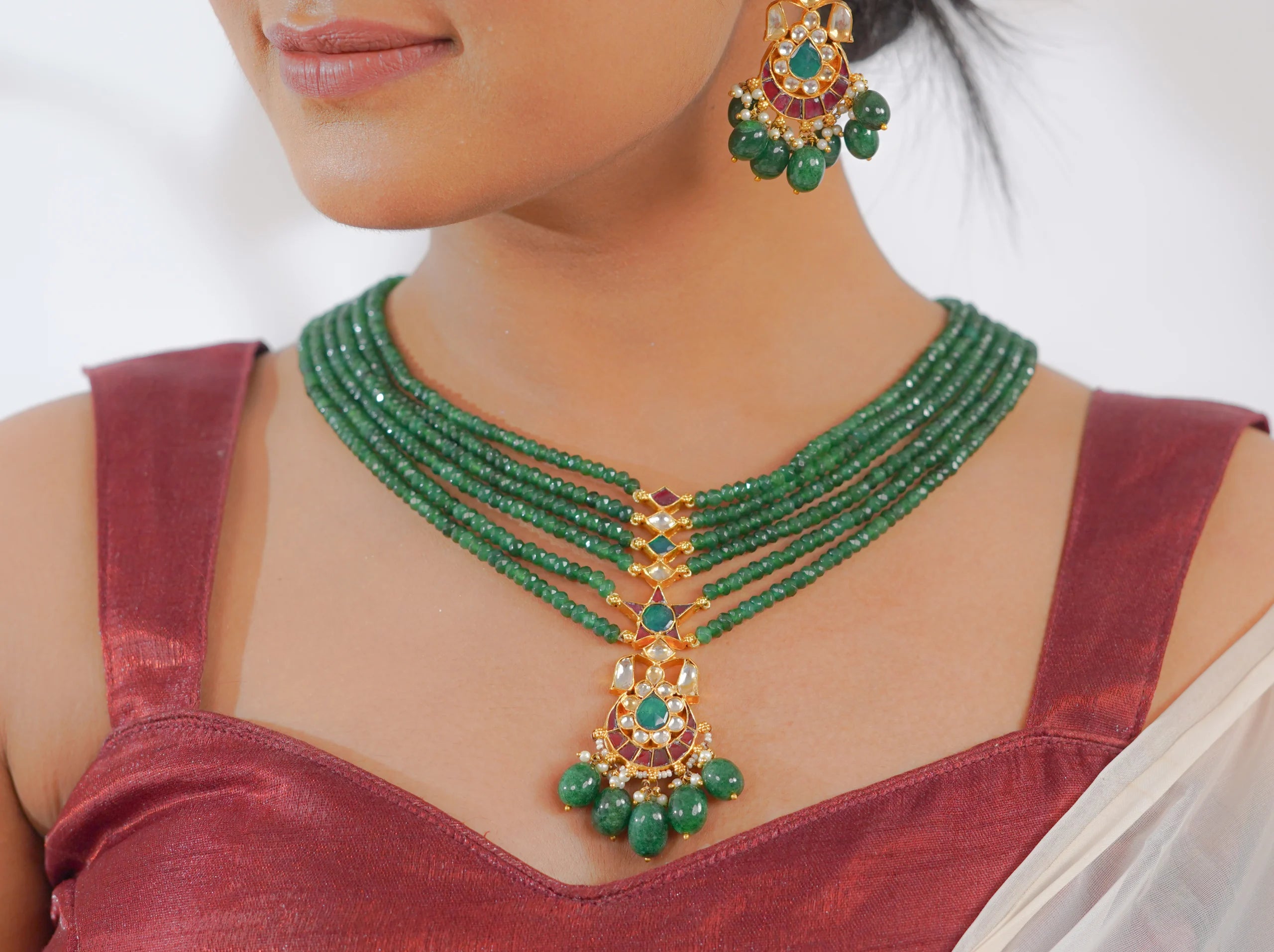 Elegant green gemstone necklace and matching earrings with gold and pearl accents, worn with a red saree.