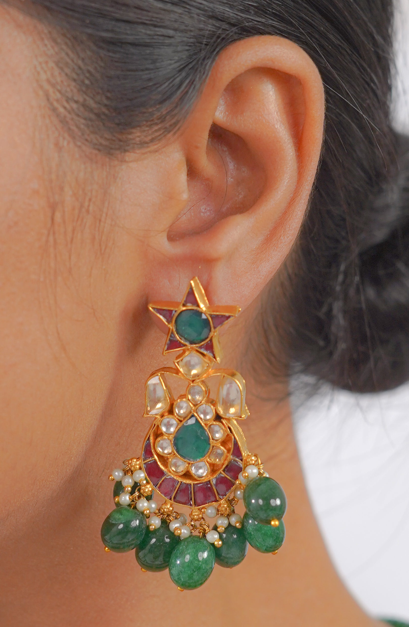 Gold jhumka earring with green emerald, red stone, and pearl detailing, worn on ear
